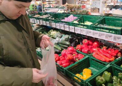 Mężczyzna wkłada warzywa do foliowej reklamówki podczas zakupów spożywczych w supermarkecie.