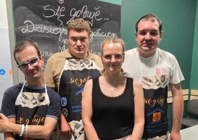 Trzech mężczyzn i jedna kobieta pozują do zdjęcia. Mężczyźni ubrani są w fartuchy kulinarne.