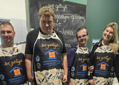 Trzech uczestników ŚDS ubrani w fartuchy kulinarne pozują do zdjęcia z zaproszonym gościem- panią Magdaleną Woch - dyrektorką Teatru im. Adama Mickiewicza w Częstochowie