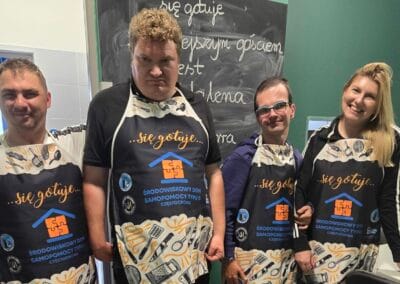 Trzej uczestnicy pozują do zdjęcia z zaproszonym gościem - Magdaleną Woch. Wszyscy mają ubrane kuchenne fartuchy.