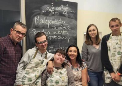 Trzej uczestnicy - dwaj mężczyźni oraz kobieta - pozują do zdjęcia z zaproszoną Małgorzatą Iżyńską oraz z Prezesem Stowarzyszenia i kadrą.