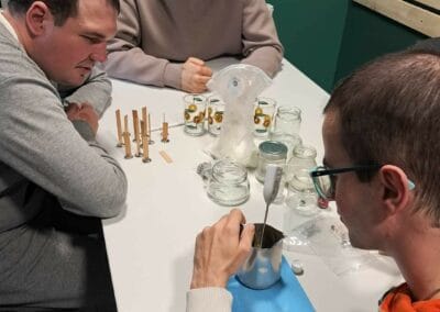 Trzech mężczyzn siedzi przy stole podczas zajęć. Jeden z nich mierzy termometrem temperaturę wosku