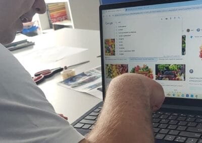 Mężczyzna używa laptopa. Wyszukuje informacje przy użyciu przeglądarki. Ma uniesioną dłoń, jest w trakcie wpisywania tekstu na klawiaturze.