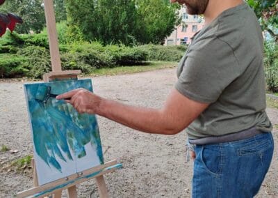 Mężczyzna stojąc w plenerze maluje wałkiem tło na płótnie.
