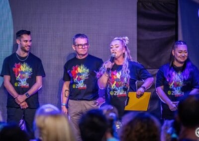 Cztery osoby ( dwie kobiety i dwóch mężczyzn) stoją na scenie w trakcie wydarzenia "Tanecznym krokiem w niebieski świat autyzmu". Jedna z kobiet zwraca się do publiczności przez mikrofon.