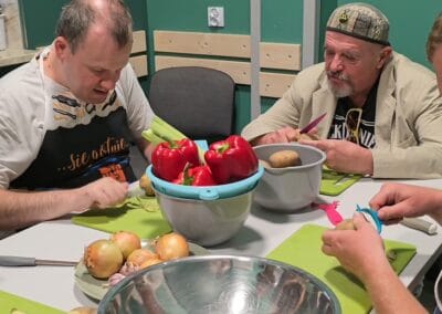 Dwóch mężczyzn siedzi przy stole i obierają ziemniaki.