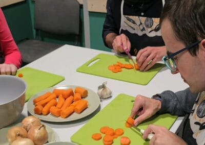 Dwóch mężczyzn kroi marchewkę na desce kuchennej.