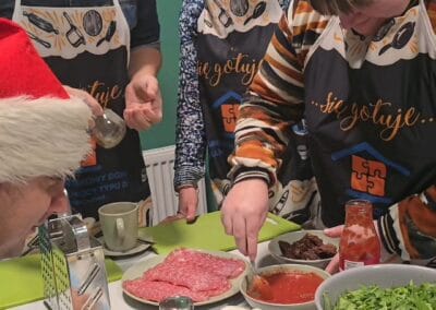 Kobieta miesza w miseczce sos pomidorowy. Trzy pozostałe osoby przyglądają się tej czynności.