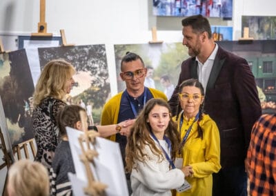 W centrum zdjęcia znajdują się Damian Drewniak z żoną Katarzyną i córką oraz Piotr Gruszka. Za nimi można dostrzec sztalugi, które prezentują zdjęcia z Kalendarza WnętrzoSłowa.