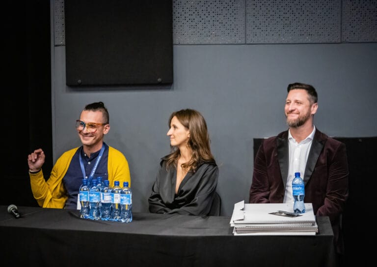 Przy stole na scenie siedzą uśmiechnięci Damian Drewniak, Aleksandra Szettel-Gruszka oraz Piotr Gruszka.