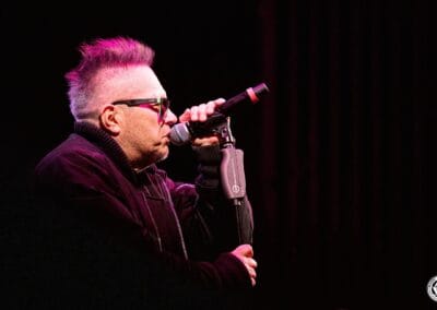 Zdjęcie przedstawia Muńka Staszczyka, który w dłoni trzyma mikrofon i śpiewa.