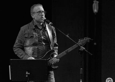 Na zdjęciu widoczny jest muzyk - Krzysztof Niedźwiecki. Mężczyzna trzyma w rękach gitarę, przy użyciu mikrofonu zwraca się do publiczności.