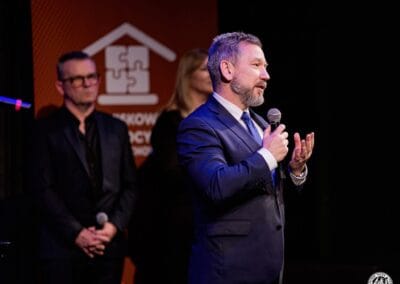 Na pierwszym planie widoczny jest mężczyzna (Adam Zaczkowski, I Wicewojewoda Śląski) wypowiadający się przy użyciu mikrofonu w kierunku publiczności. Na drugim planie - Prezes Stowarzyszenia Daj mi czas oraz Dyrektor Teatru im. Adama Mickiewicza.