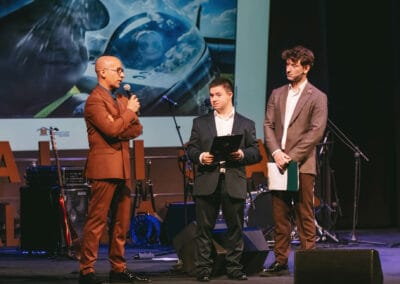 Na zdjęciu widocznych jest trzech mężczyzn - dwóch prowadzących galę prezentacji kalendarza "Barwy Sportu okiem Skowronka" oraz fotograf - Grzegorz Skowronek, który wypowiada się przy użyciu mikrofonu. Wszyscy mężczyźni stoją na scenie teatralnej, za nimi widoczny jest ekran, wyświetlający zdjęcie z jednej ze stron kalendarza.