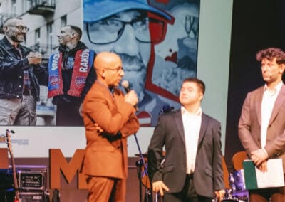 Na zdjęciu widocznych jest trzech mężczyzn - dwóch prowadzących galę prezentacji kalendarza "Barwy Sportu okiem Skowronka" oraz fotograf - Grzegorz Skowronek, który wypowiada się przy użyciu mikrofonu. Wszyscy mężczyźni stoją na scenie teatralnej, za nimi widoczny jest ekran, wyświetlający zdjęcie z jednej ze stron kalendarza.