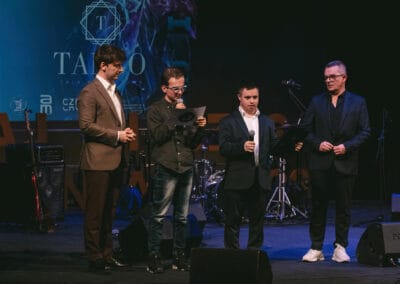 Na zdjęciu widocznych jest czterech mężczyzn - dwaj prowadzący galę prezentacji kalendarza "Barwy Sportu okiem Skowronka", prezes Stowarzyszenia Daj mi czas oraz podopieczny tego stowarzyszenia, który czyta tekst.